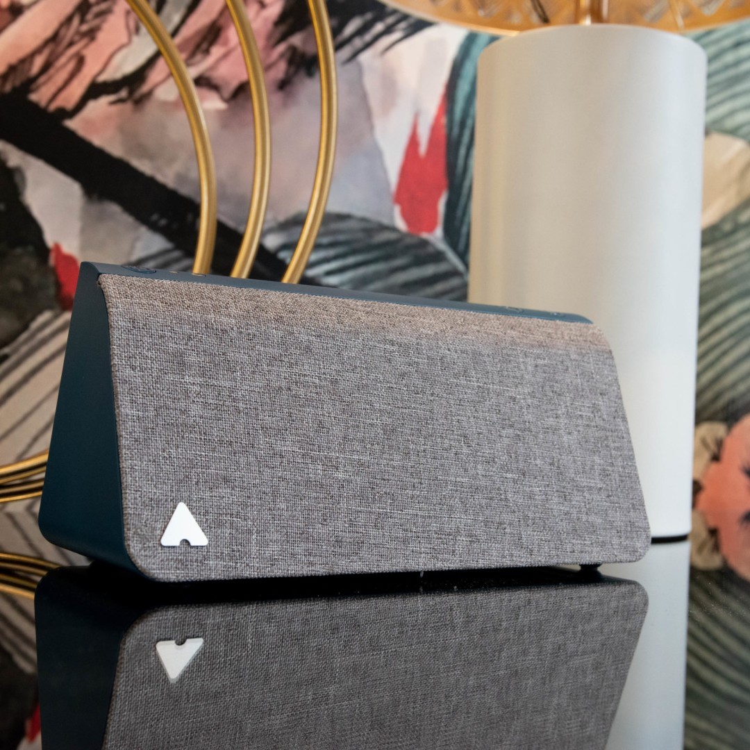 A smart home device shaped like an extruded triangle, with the logo mark in the corner.